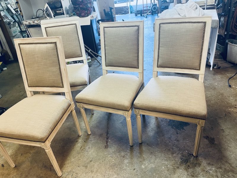 A set of cream linen dining chairs with brass nailhead trim