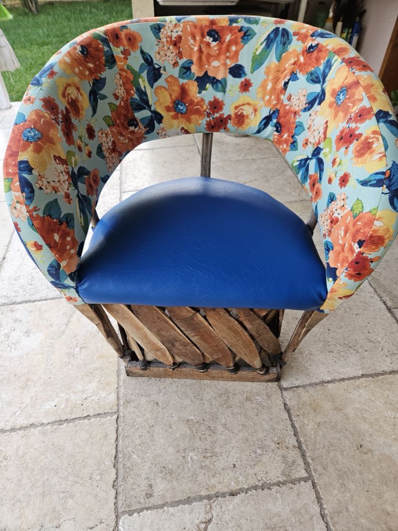 A round barrel chair reupholstered in bright orange-and-blue floral fabric with a blue leather seat